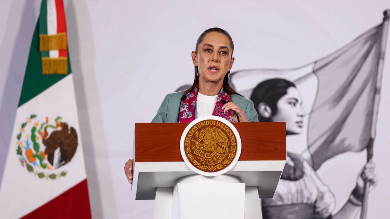 Person speaking at a podium with Mexican flag nearby.