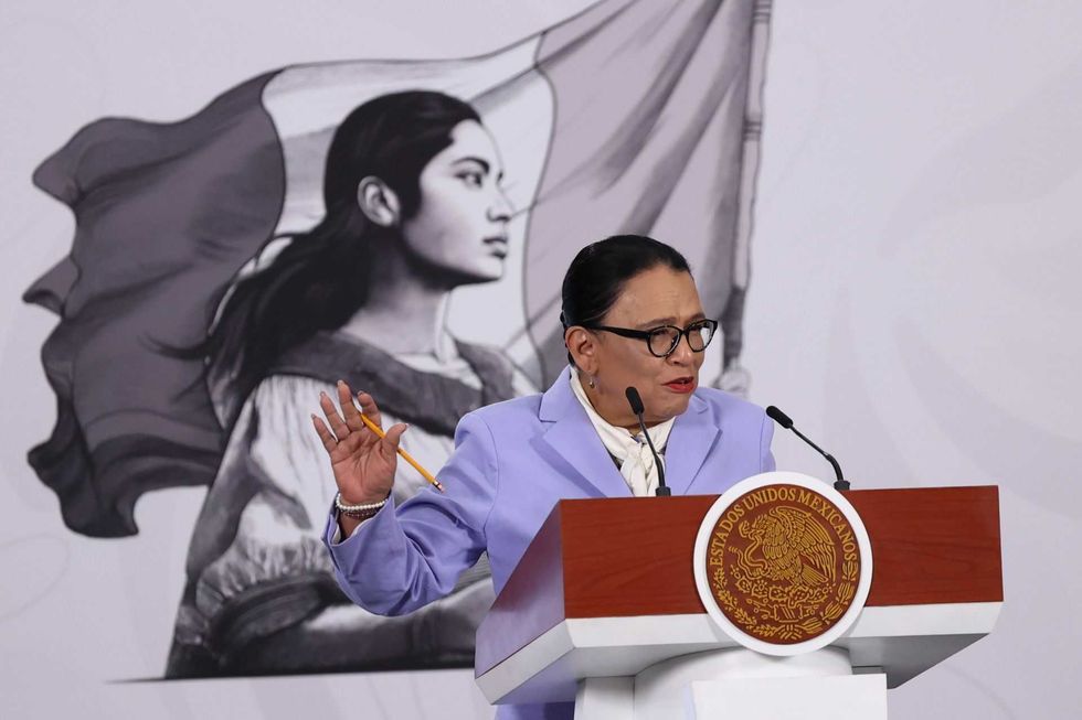 Person speaking at podium with large portrait and flag in background.