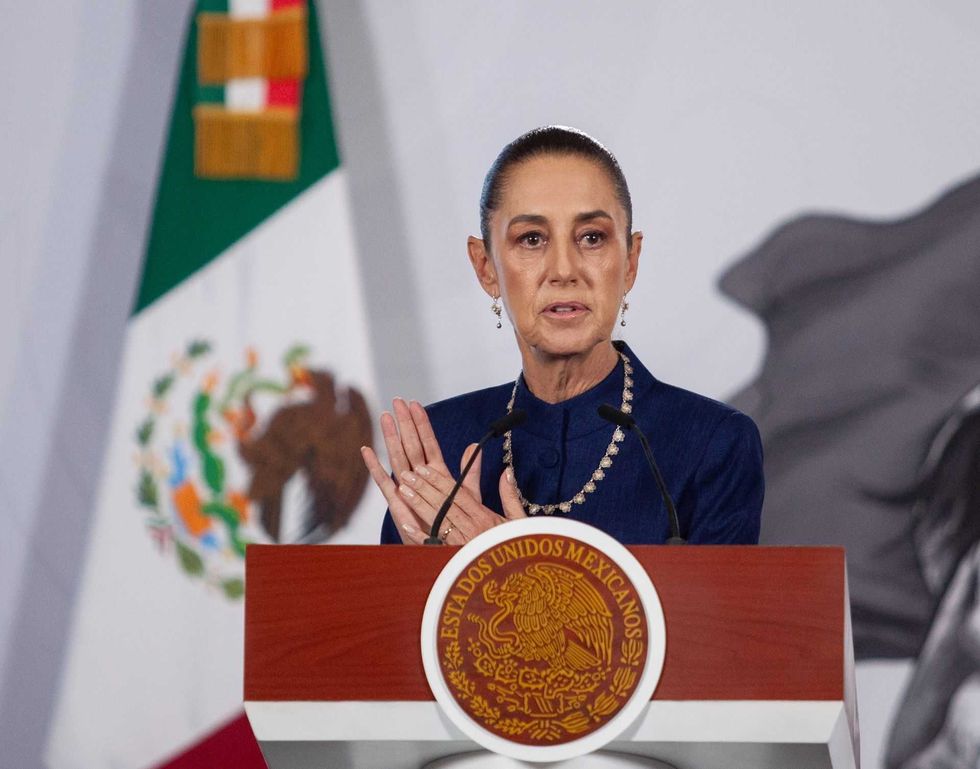 Person speaking at podium with Mexican flag in background.