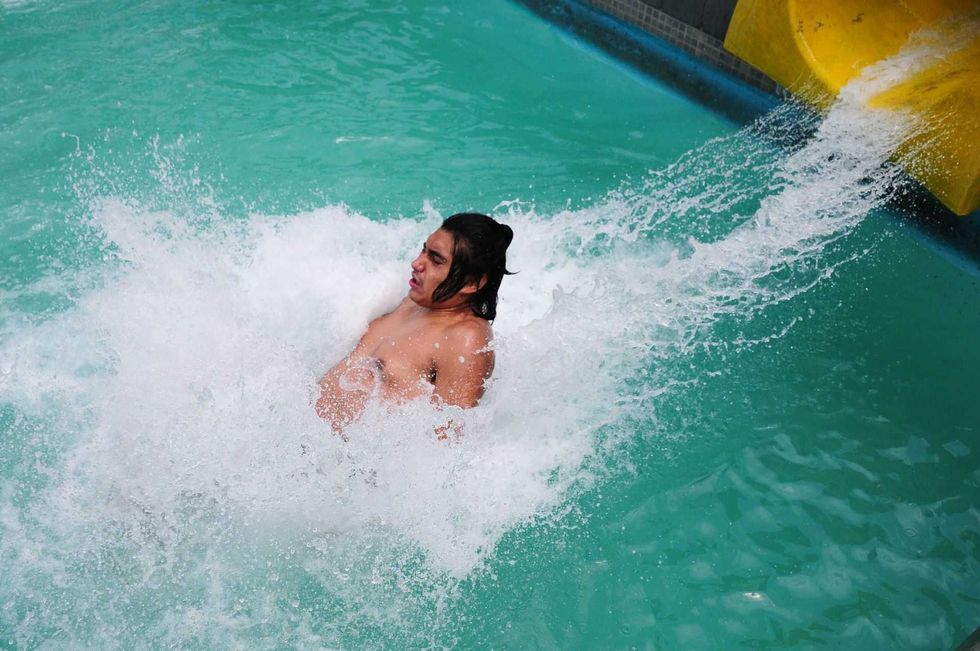 Person splashing into a pool from a yellow waterslide, creating a big splash.