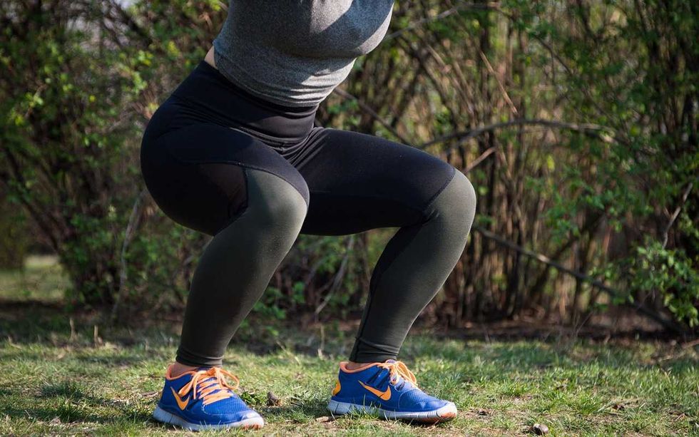 Person squatting outdoors in athletic leggings and blue sneakers.