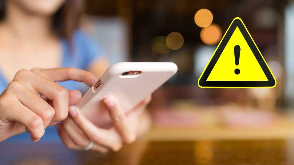 Person using a smartphone with a warning sign overlay.
