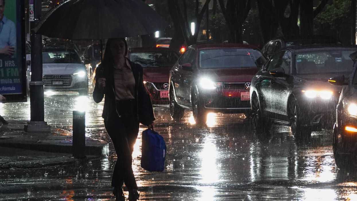 Person walking under an umbrella in the rain with cars and headlights in the background.