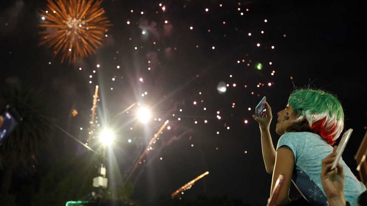 Person watching fireworks at night, holding a phone, with colorful hair.
