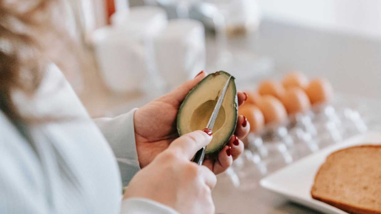 Persona cortando un aguacate con un cuchillo mientras lo sostiene con la mano