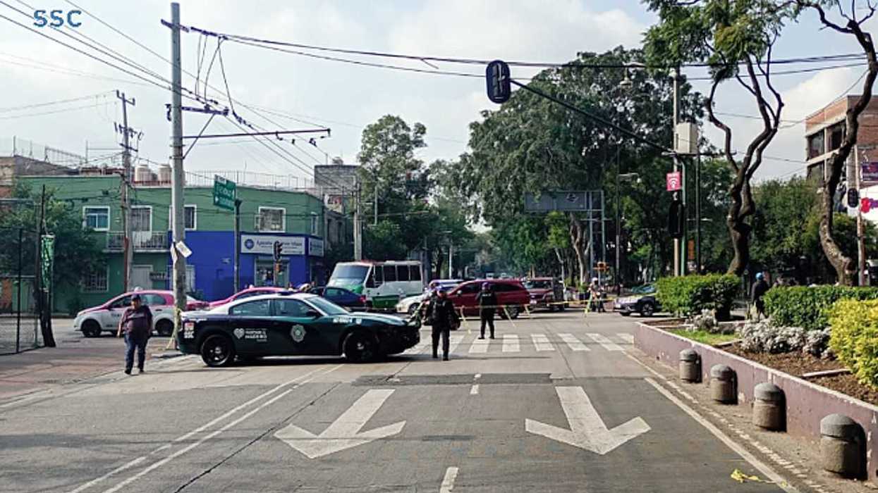 Police cars block an intersection, diverting traffic; officers and caution tape visible.