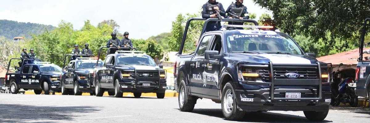 Police convoy of black pickup trucks driving down a street.