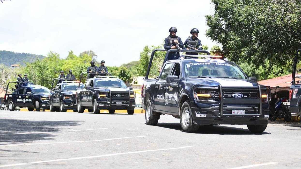 Police convoy of black pickup trucks driving down a street.