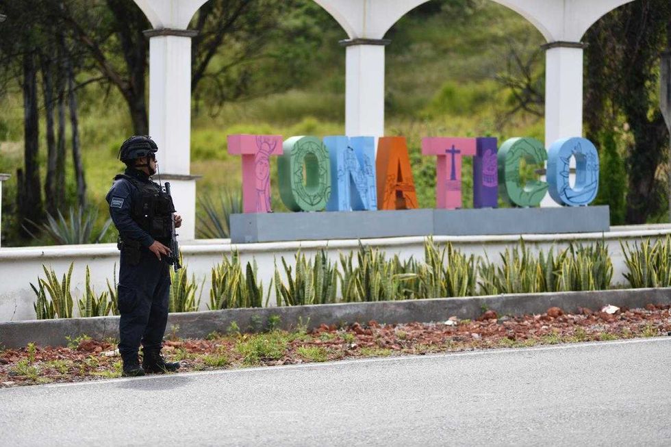 Police officer stands by colorful "TONATICO" sign on a roadside.