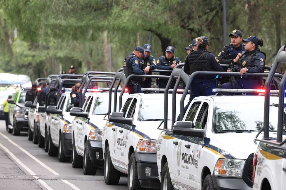 Police officers standing on parked patrol vehicles in a line on a tree-lined street.