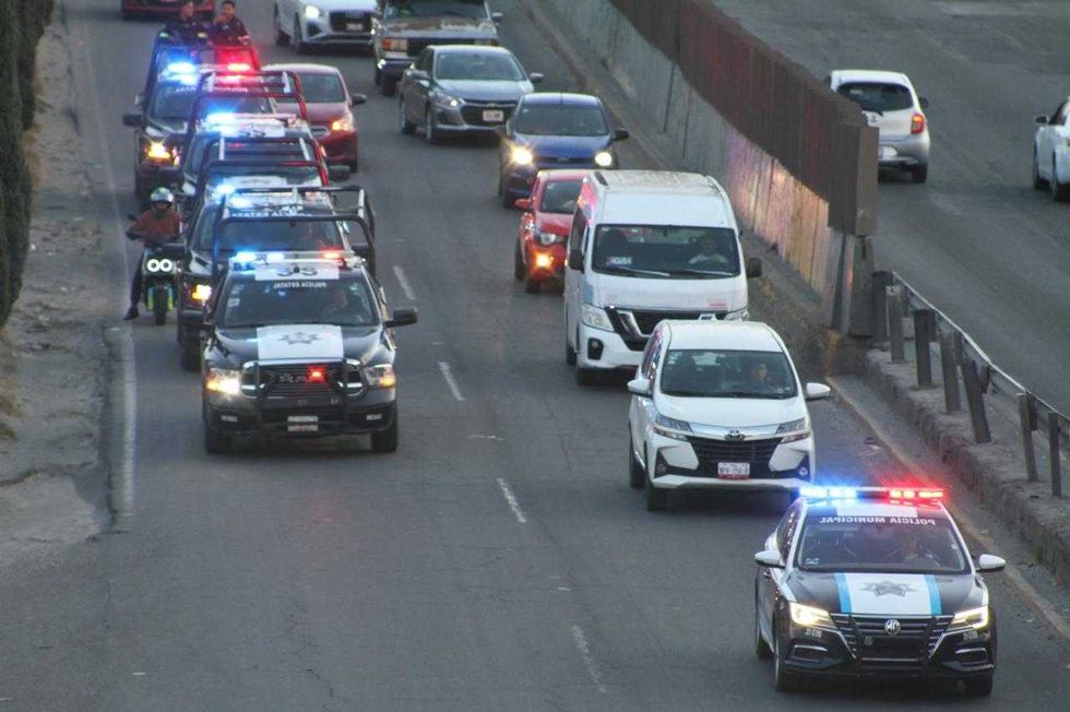 Police vehicles with flashing lights escort a convoy on a highway.