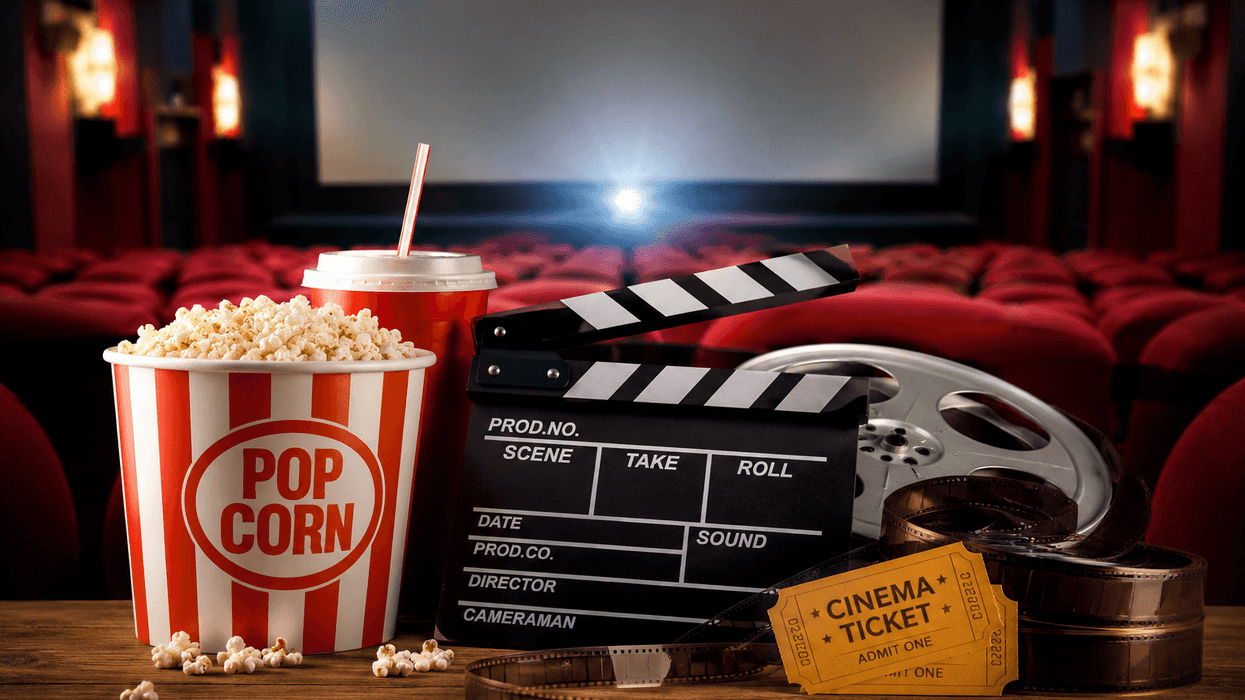 Popcorn, drink, clapperboard, and film reel in a cinema with empty red seats.