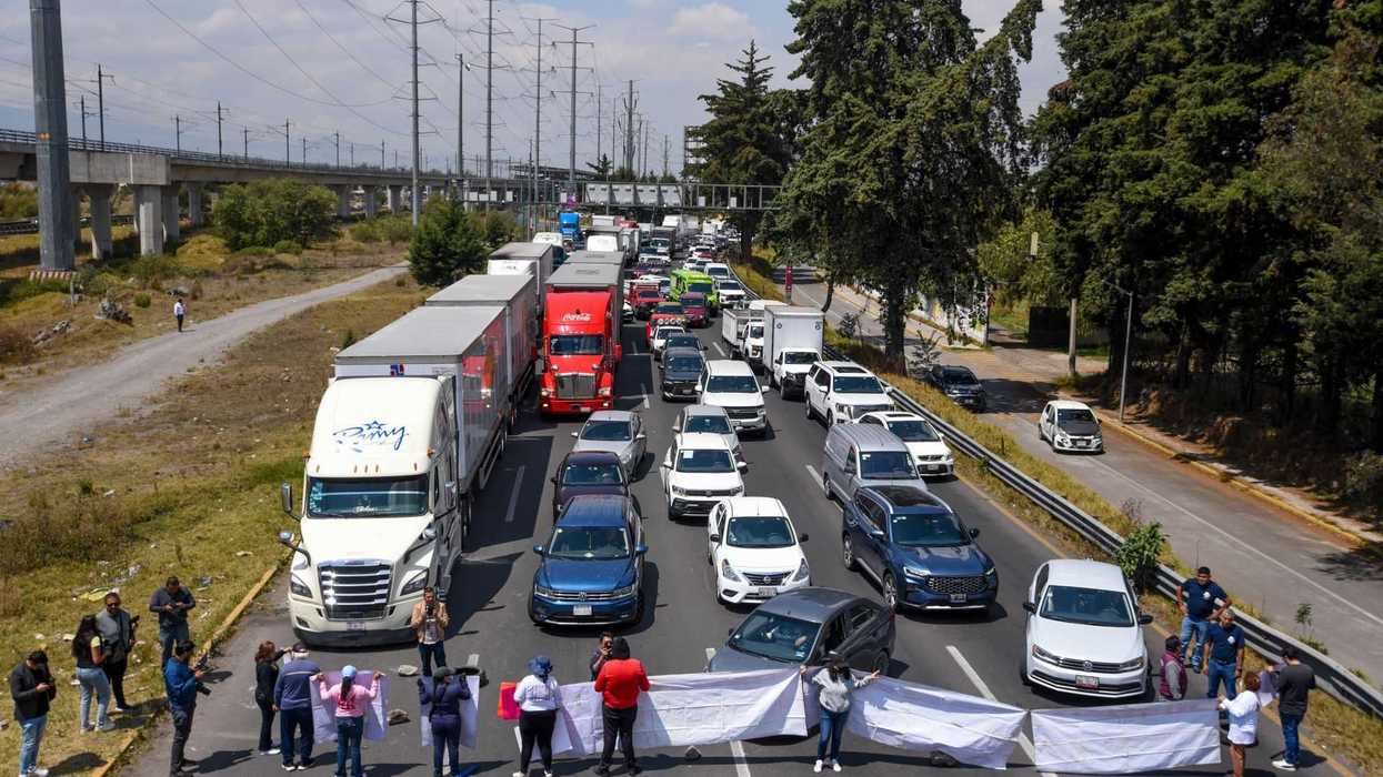 Protesters block a busy highway, holding banners, causing a traffic jam.