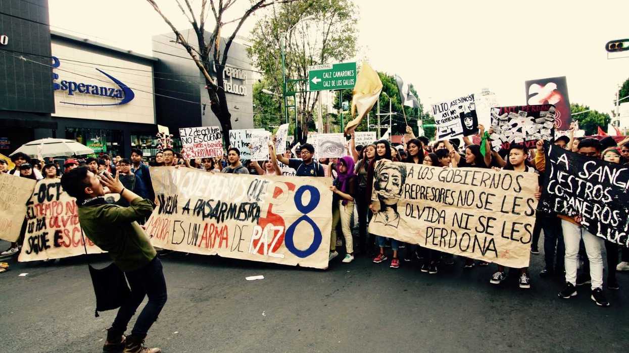 Protesters hold signs, gathered on a street, one person leads a chant.