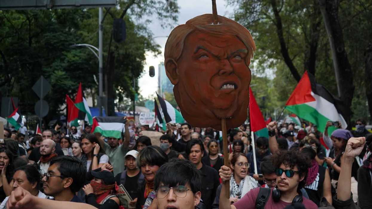 Protesters march with flags and a large caricature, raising fists in solidarity.