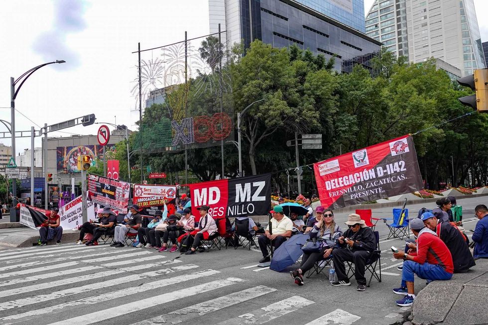 Protesters sit with banners in an urban setting, blocking a street with traffic lights.