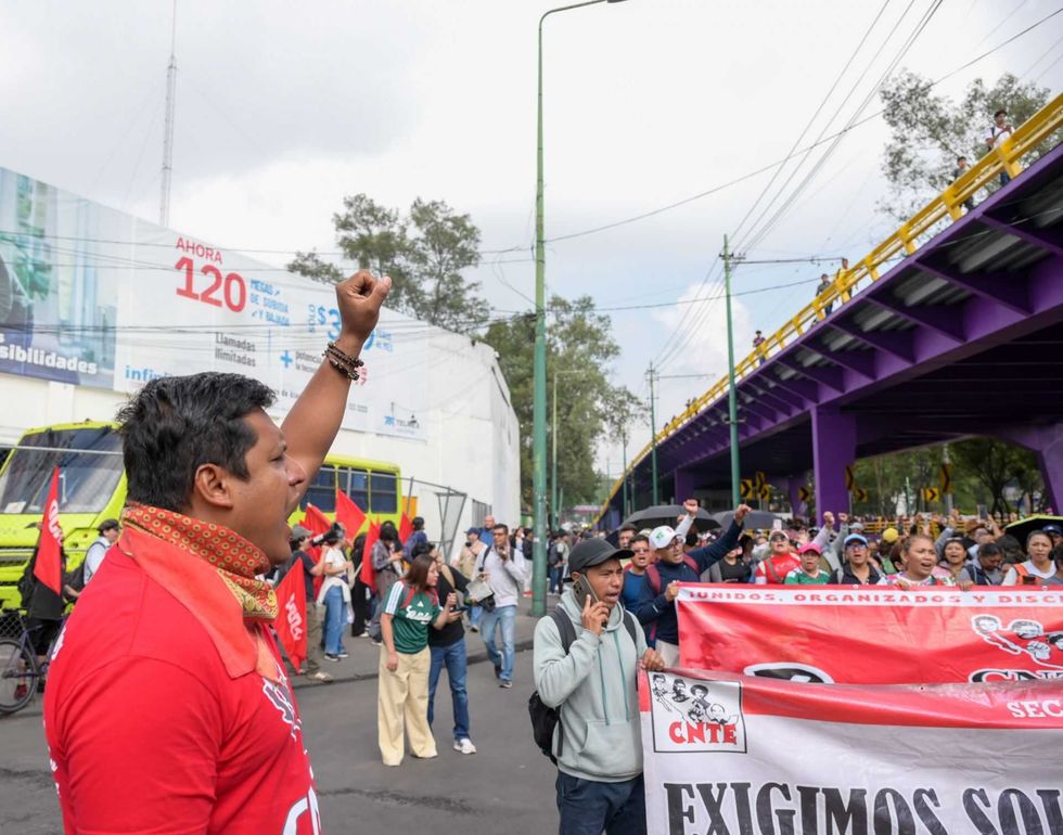 Protesters with banners and raised fists march under a purple bridge.