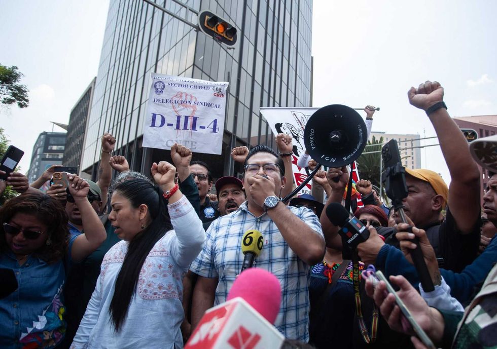 Protesters with raised fists and a megaphone gather outside city buildings.