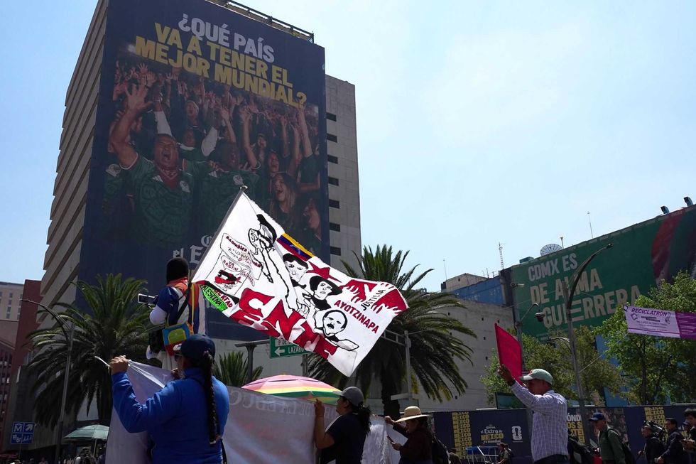 Protestors with flags in front of a large building advertisement and green mural.