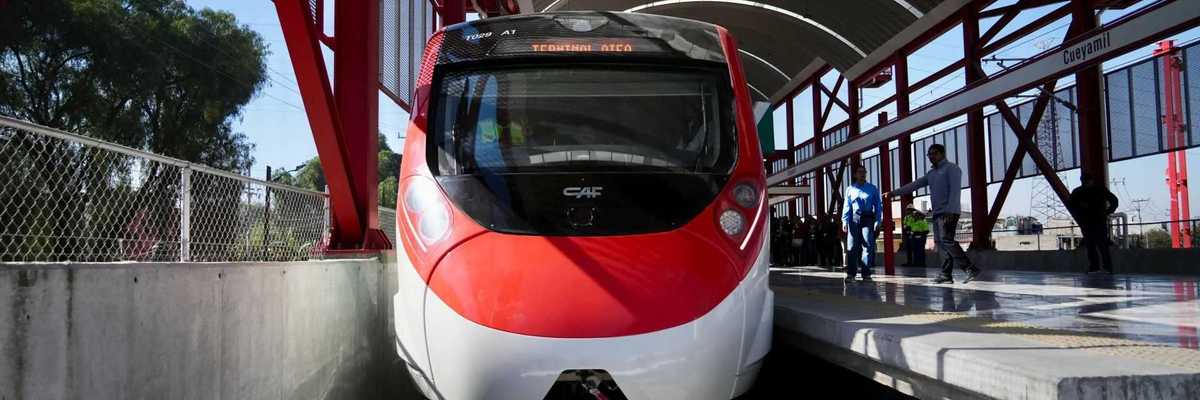 Red and white passenger train at Cueyamil station platform on a sunny day.