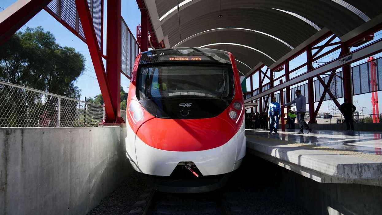 Red and white passenger train at Cueyamil station platform on a sunny day.
