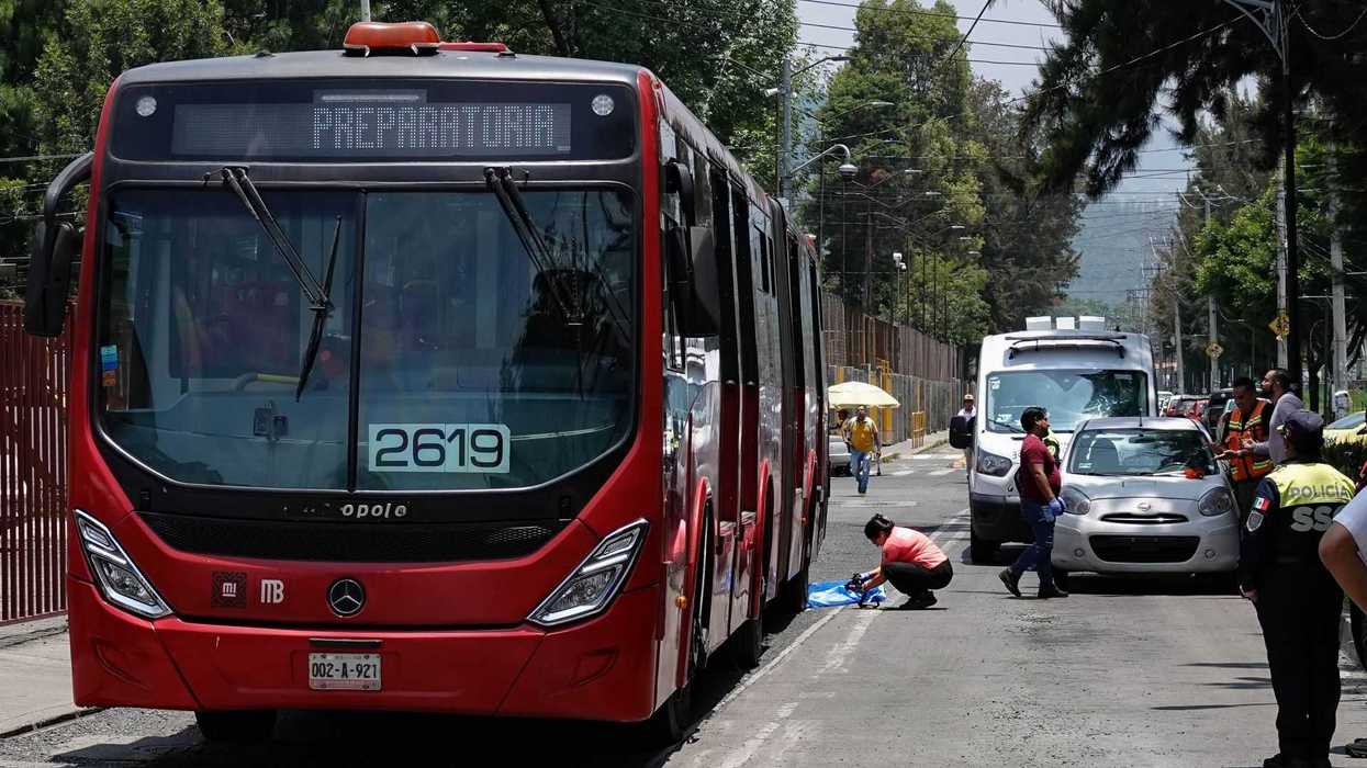 Red bus labeled "Preparatoria" on a street with police and bystanders nearby.