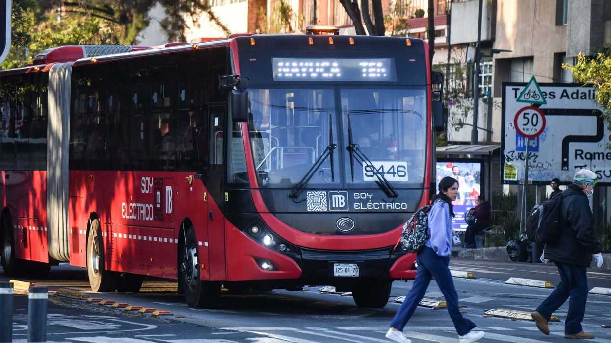 Red electric bus at a crosswalk with pedestrians in an urban setting.
