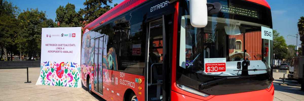 Red electric bus in a plaza with a "Quetzalcoatl" sign nearby.