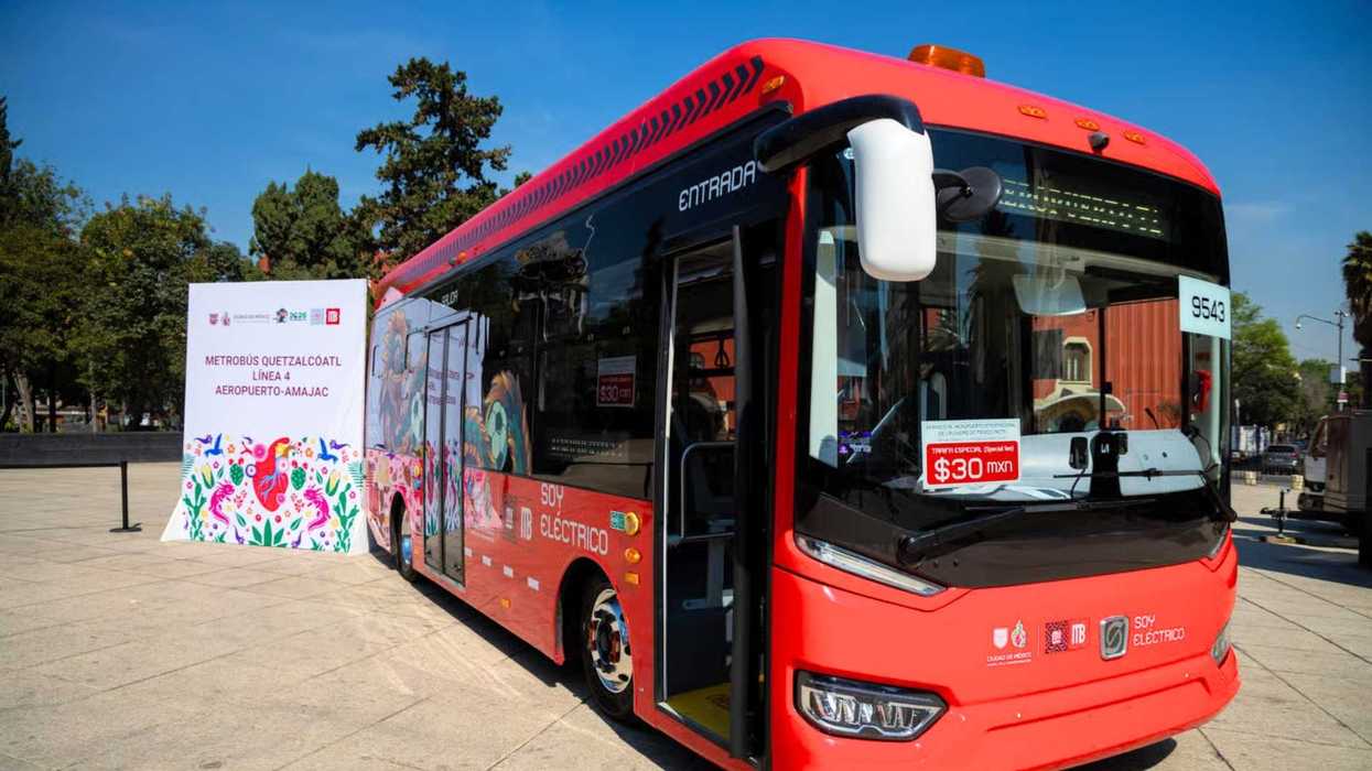 Red electric bus in a plaza with a "Quetzalcoatl" sign nearby.