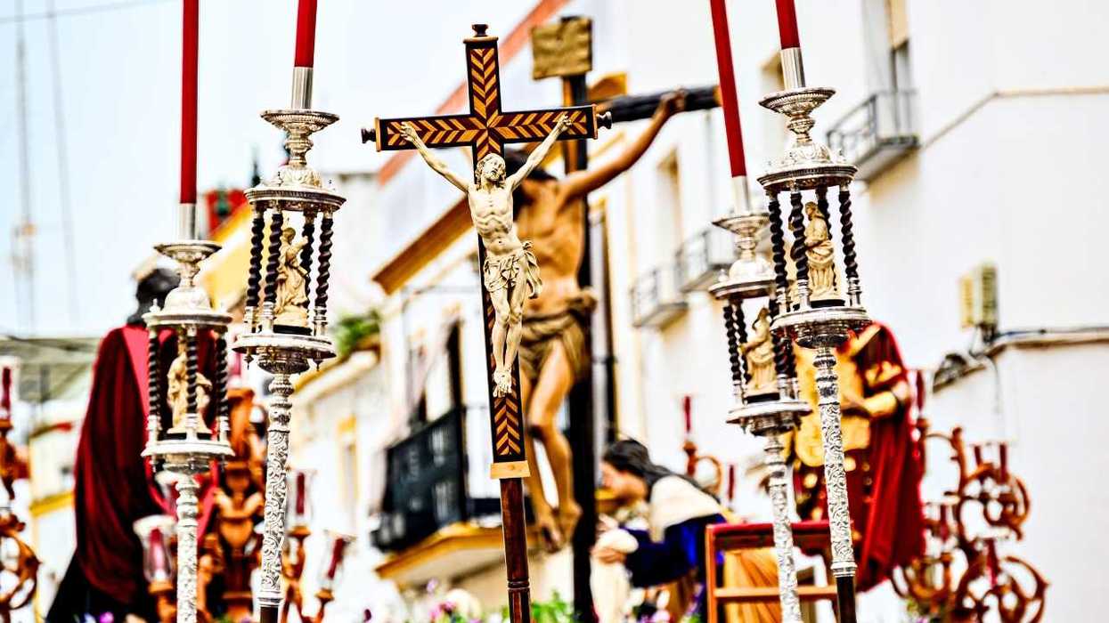 Religious parade with crucifix and ornate candle holders in a sunny street.