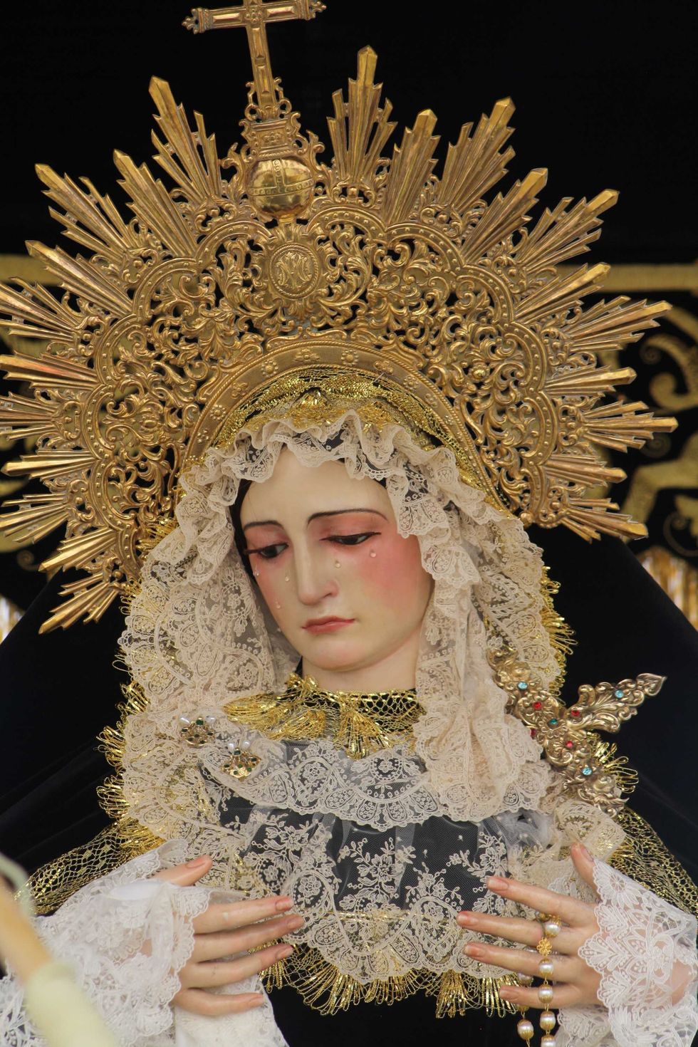 Religious statue of a woman with ornate crown, lace veil, and holding a rosary.