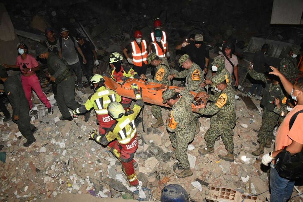 Rescue team carrying a person on a stretcher amid debris at night.