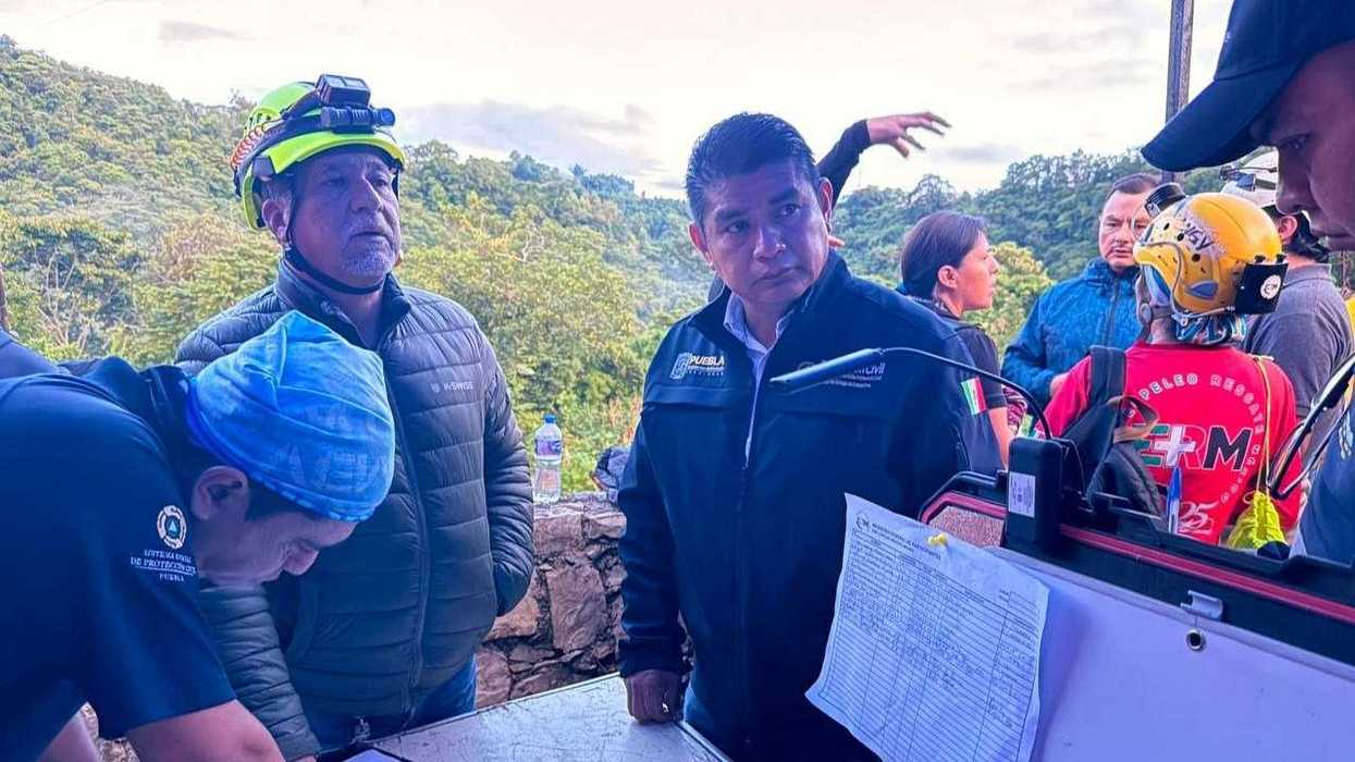 Rescue team members and officials discuss plans outdoors near a forested area.