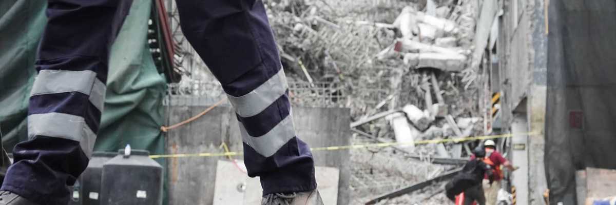 Rescue worker walking near a building collapse site with debris in the background.