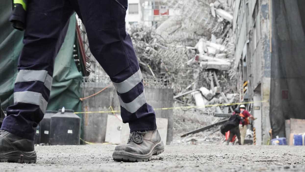 Rescue worker walking near a building collapse site with debris in the background.
