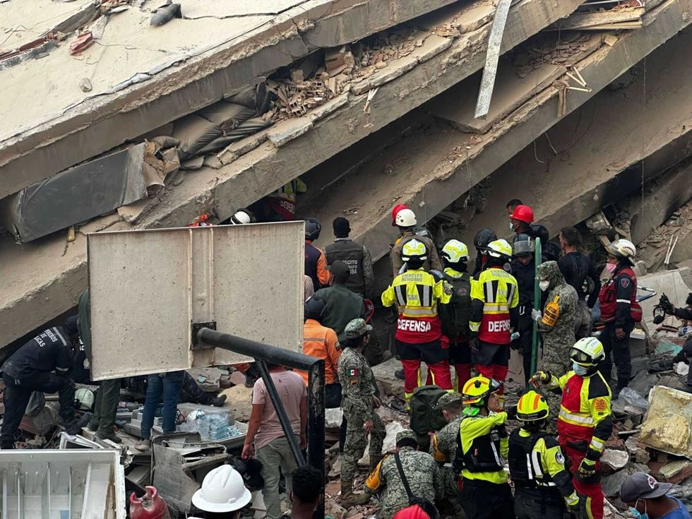 Rescue workers at a collapsed building scene with debris and equipment visible.
