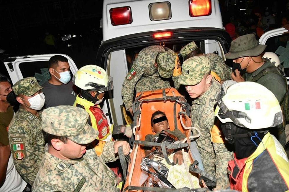 Rescue workers escort a child on a stretcher to an ambulance at night.