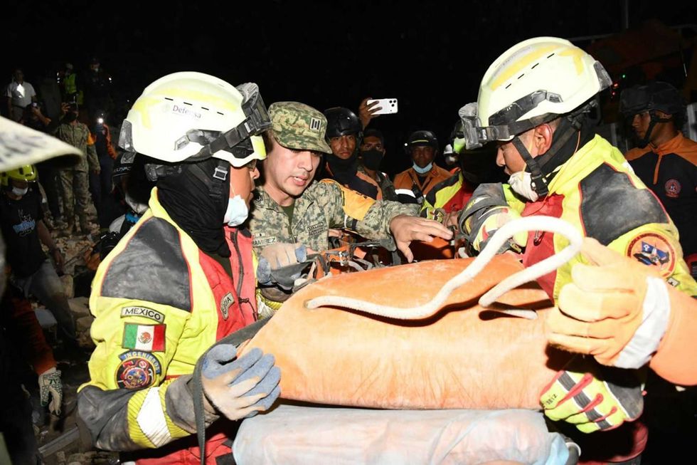 Rescue workers in helmets carry a person on a stretcher at night.