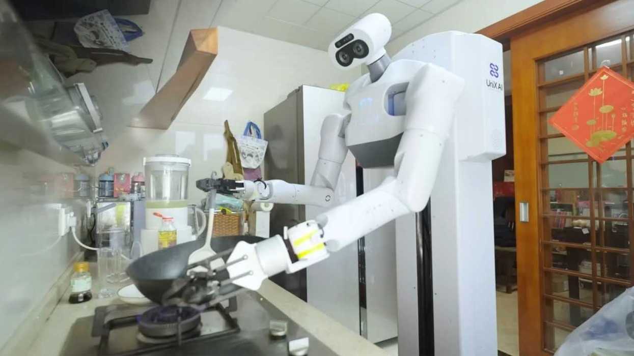Robot in kitchen cooking with a frying pan on a stove.