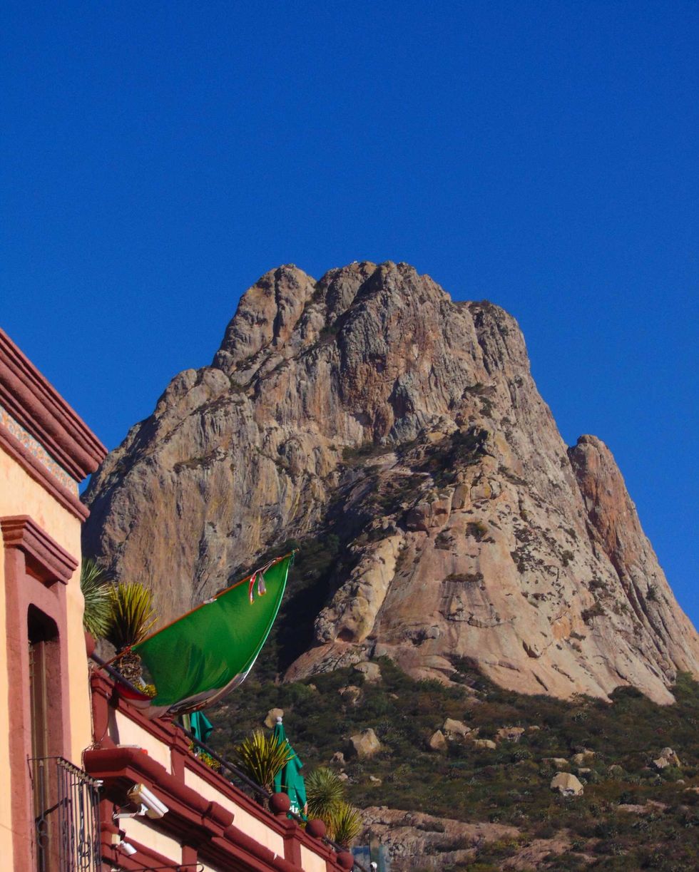 Rocky mountain peak under clear blue sky, with a building and green flag in the foreground.