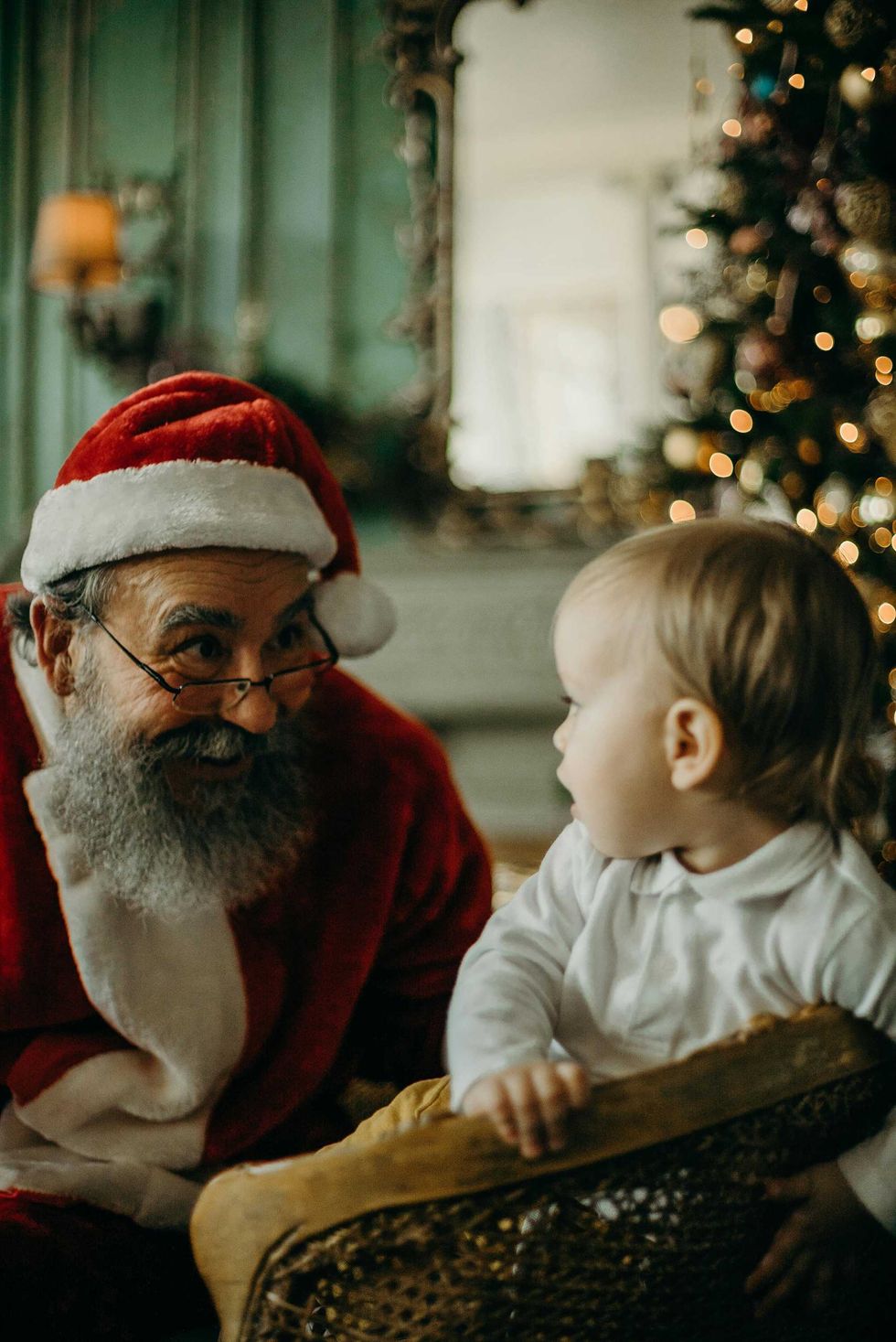 Santa Claus smiling at a baby near a Christmas tree.