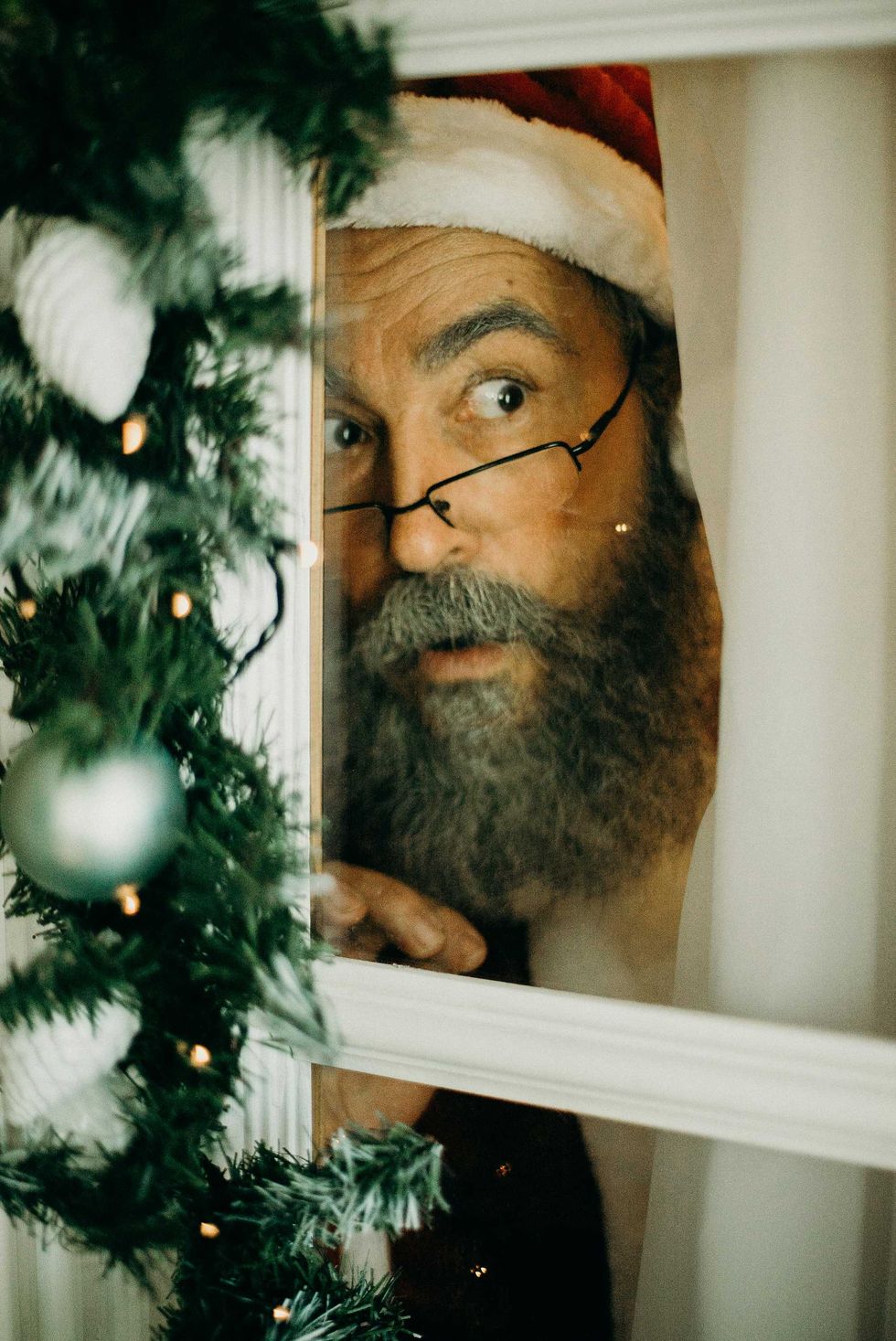 Santa peeking through a window, surrounded by Christmas garland.