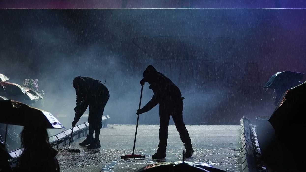 Silhouetted workers with brooms clearing rainwater from a stage.