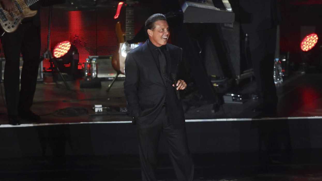 Singer in a black suit performing on stage with musicians and red lights.
