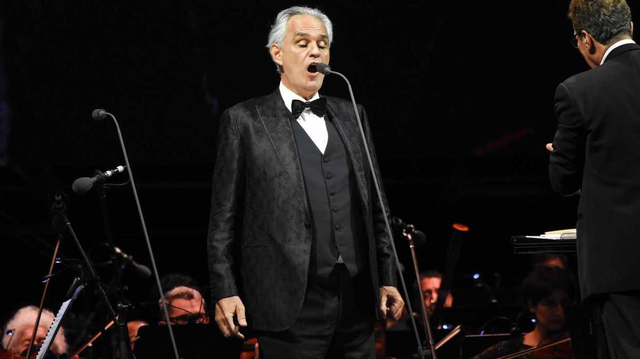Singer in a tuxedo performs with an orchestra on stage.