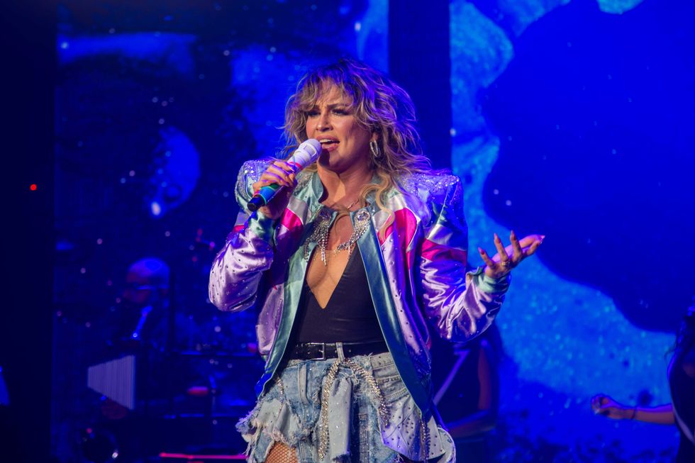 Singer performs on stage in a colorful outfit, holding a microphone.