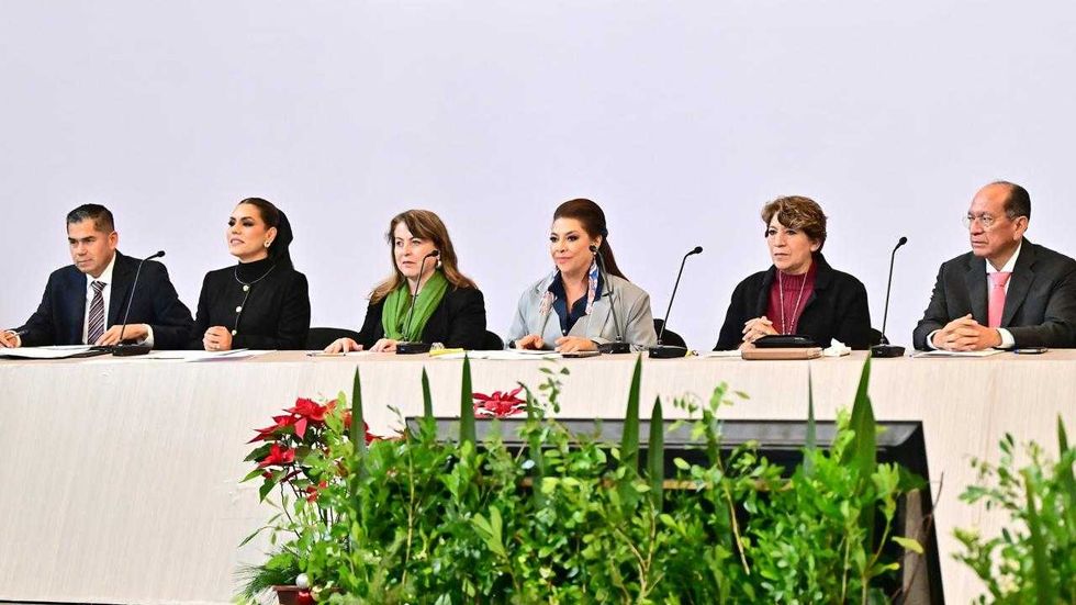 Six people seated at a panel table, with plants in the foreground.