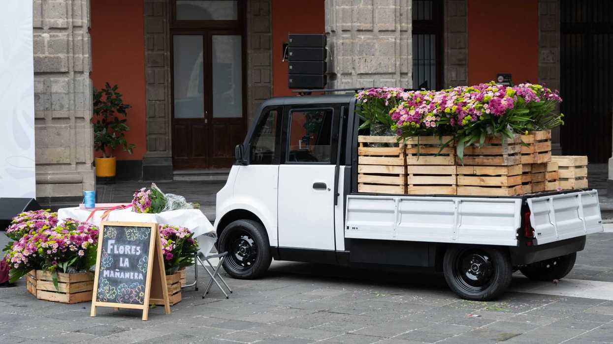 Small truck with flower crates next to a table and a sign in a courtyard.