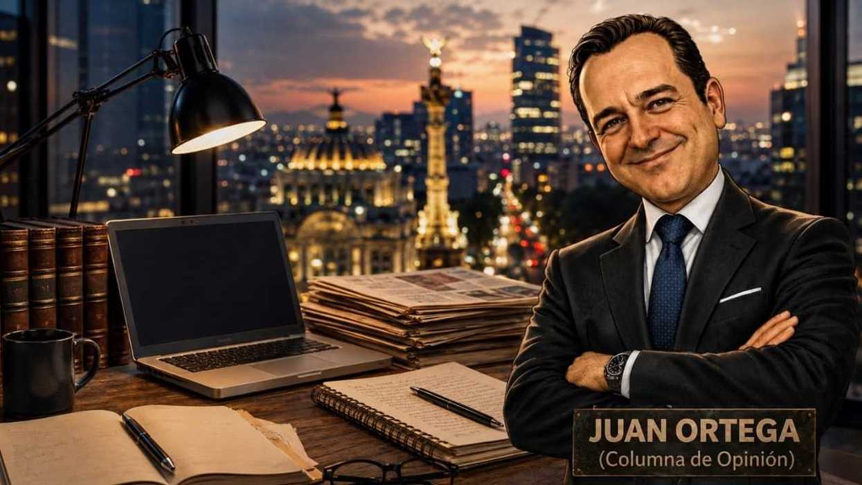 Smiling man in office with laptop, books, and cityscape backdrop at dusk.