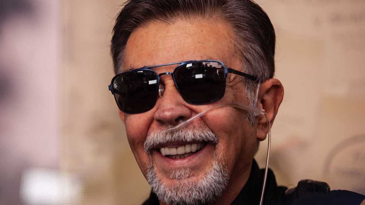 Smiling man with sunglasses and oxygen tubing, wearing a black shirt.